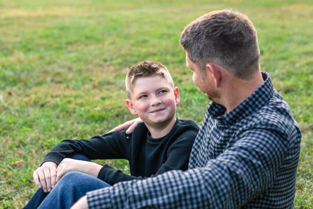 Son looking up at his father both sitting in grass
